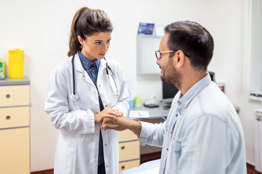 Enfermera en tópico sosteniendo la mano a un paciente preguntando sobre su estado de salud